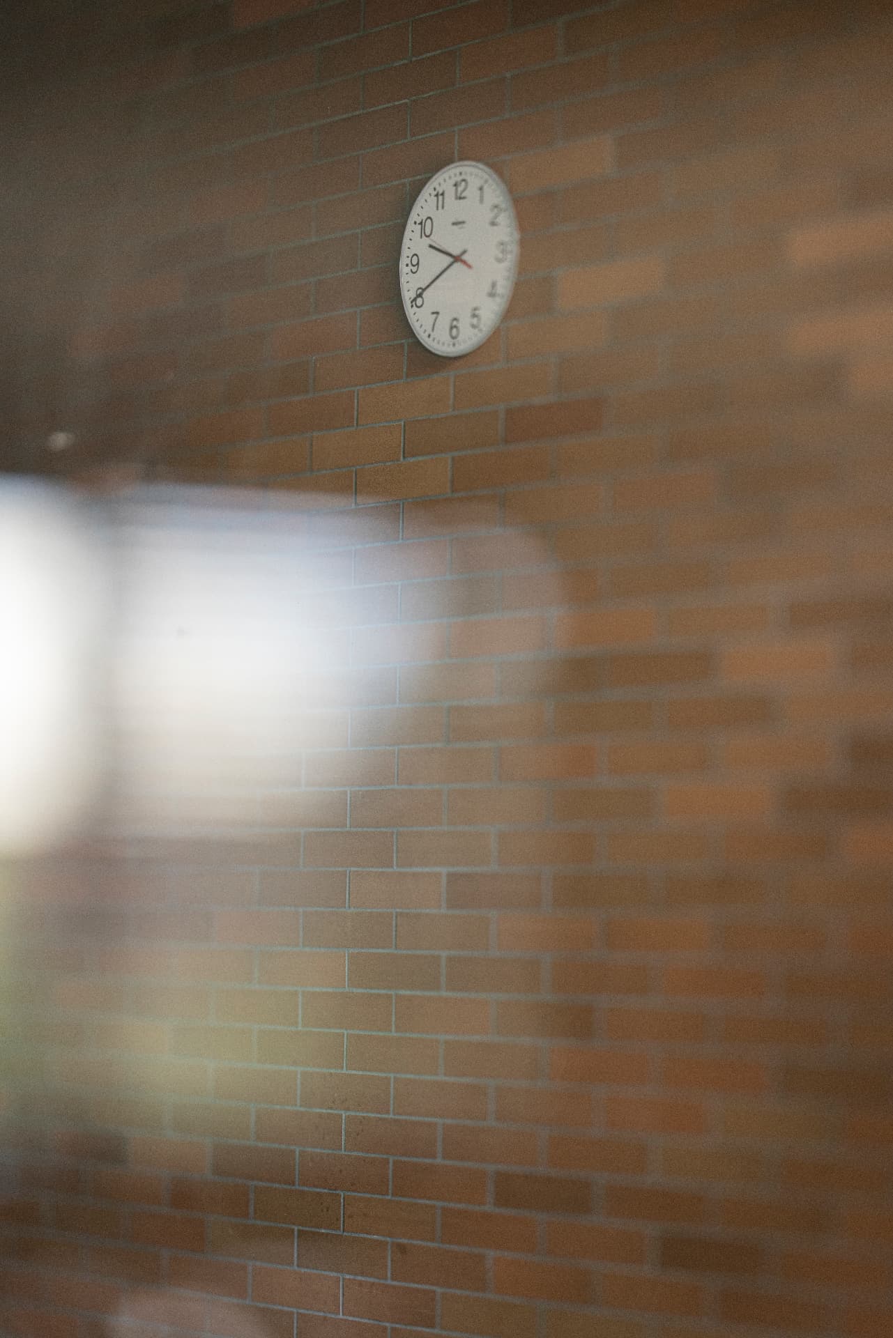 Clock on a brick wall seen through a softly blurred glass pane