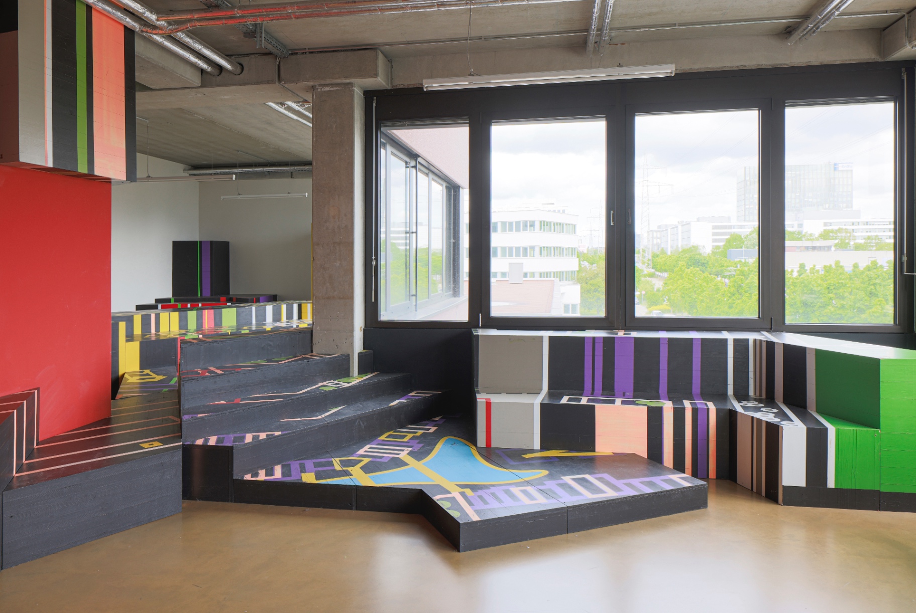 Colourful painted stepped installation with red wall and Stuttgart skyline through windows
