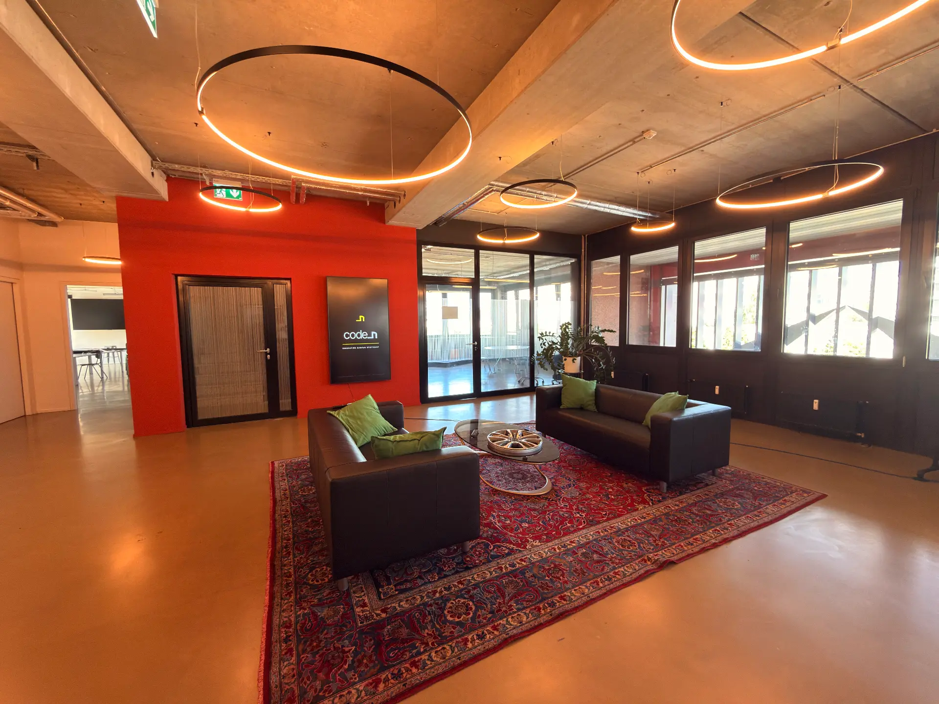 Foyer im 2. OG mit roter Wand, code_n Schriftzug, Ledersofas und Ringleuchten