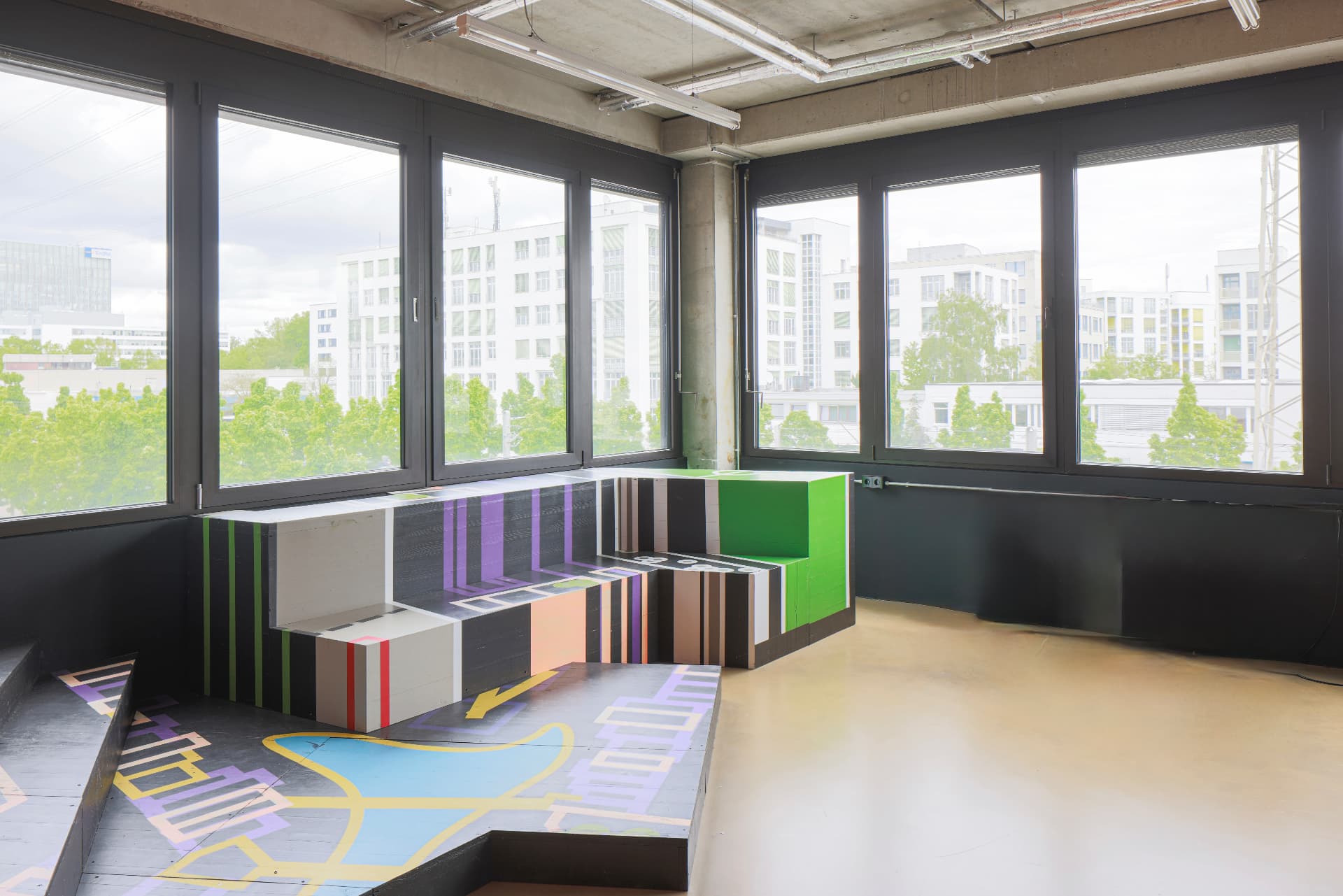 Corner room with stepped, colourfully striped seating landscape and painted city-map floor