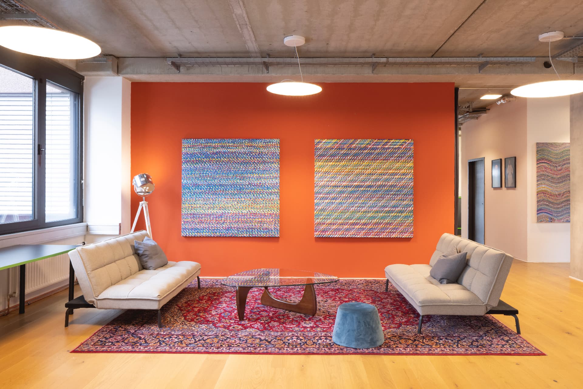 Lounge with an orange wall, two large finely dotted colour-field paintings, light sofas and a Persian rug